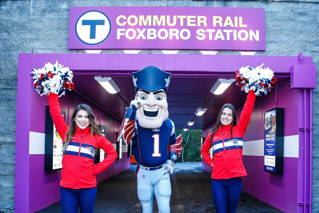 Cheerleaders on the left and right of Pat Patriot in front of the Foxboro Station's tunnel entrance